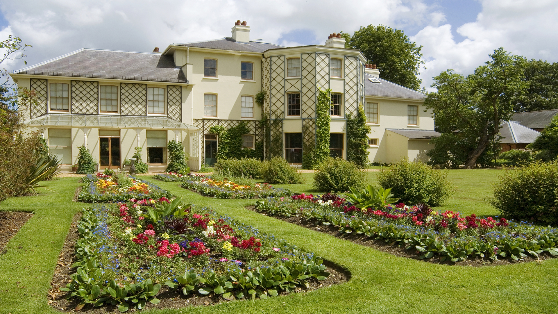 Visit the Charles Darwin House in Kent. Image courtesy of English Heritage The Down House on a bright day with a flower garden in front of it.