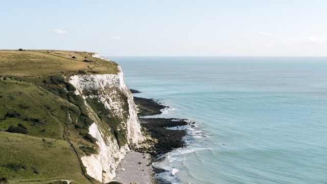 See the majestic White Cliffs of Dover. Photo by Peter Mason on Unsplash. White Cliffs of Dover plunging into the blue sea on a clear day.