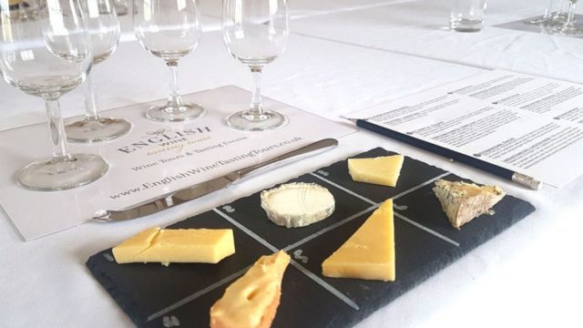Try delicious cheeses on an English Wine Tour and Tasting. Image courtesy of Golden Tours. A black slate with a selection of six cheeses next to four empty wine glasses on a wine tasting tour.