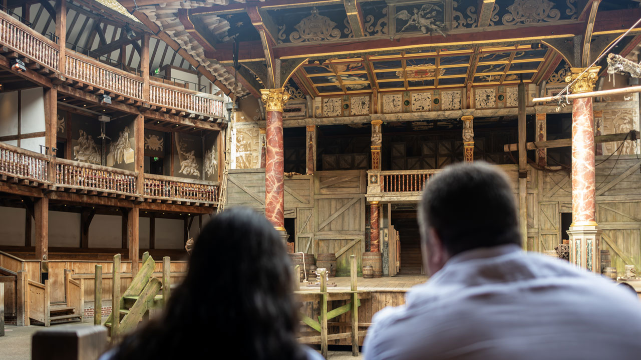 Take a guided tour of Shakespeare's Globe Theatre and marvel at the grand stage where many of Shakespeare's plays were performed over the decades. ©London & Partners/Michael Barrow Two people sit and admire the majestic setting of the Shakespeare Globe amphitheatre.