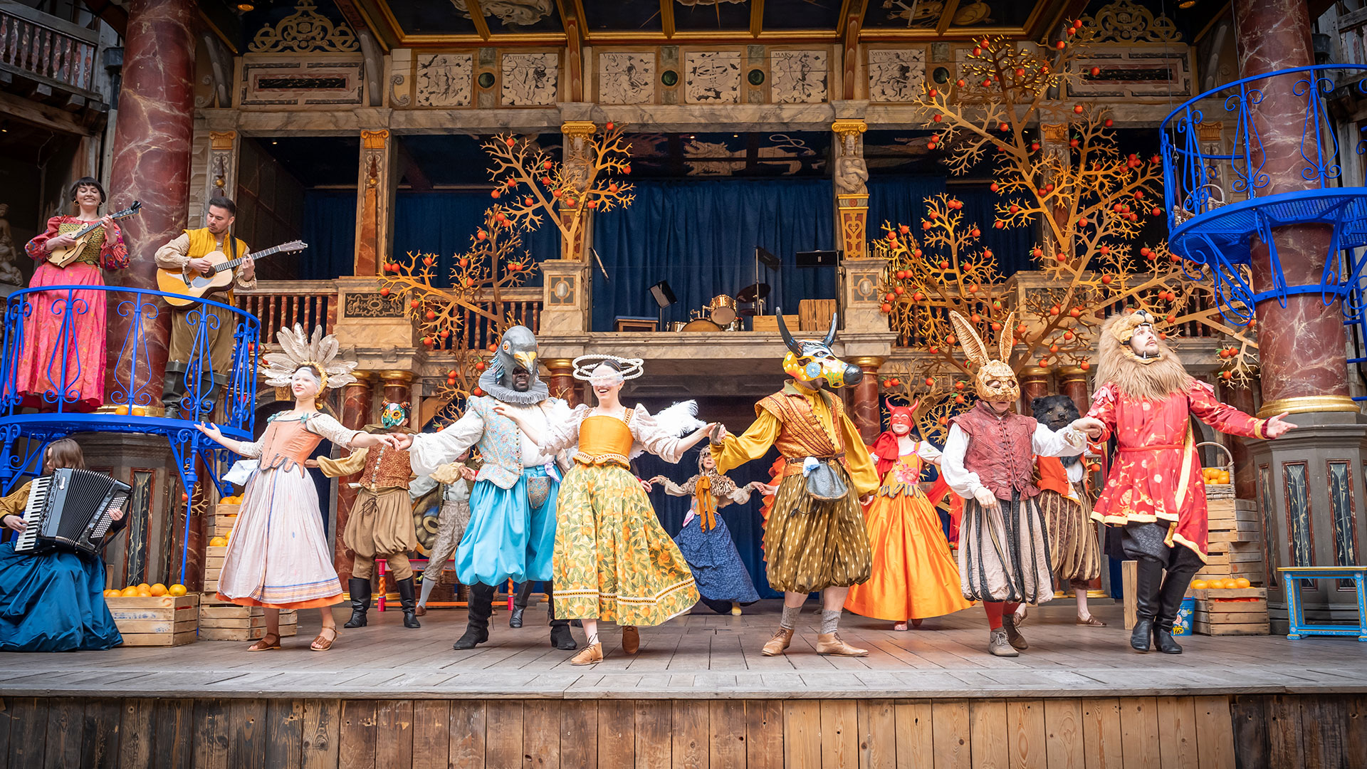 Shakespeare's Globe theatre. Image courtesy of Shakespeare's Globe. Actors wearing bright, colourful costumes and animal heads are dancing on the stage of the Shakespeare Globe Theatre.
