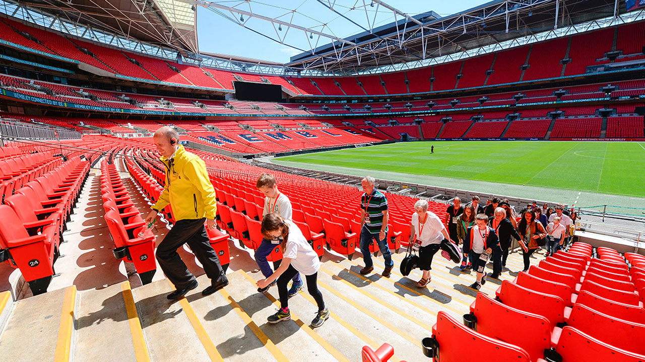 Walk in the footsteps of football and music legends on a Wembley Stadium Tour. Image courtesy of Golden Tours. Tour guide and guests walking up the steps at Wembley Stadium.