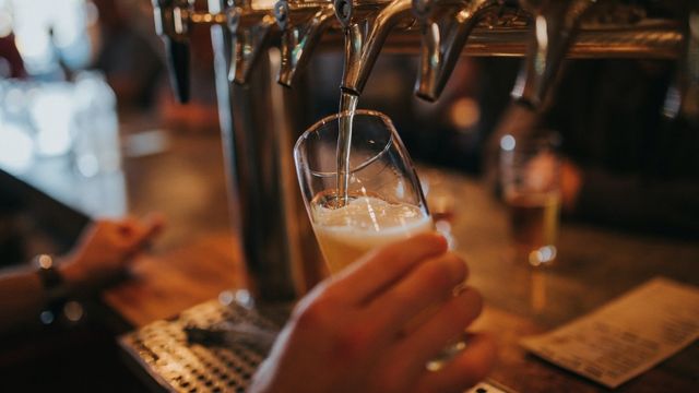 A hand holding a glass as beer comes out of a beer tap.