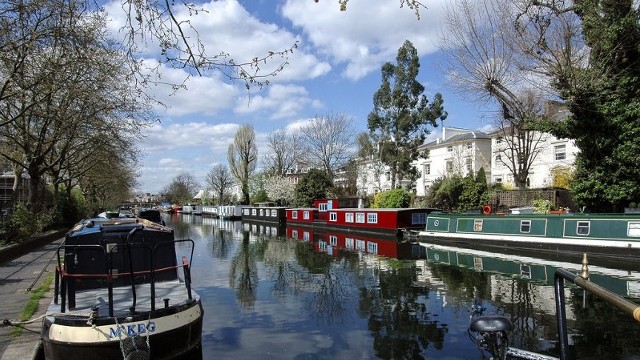 Explore canals with London Walks. Image courtesy of London Walks Looking along a canal, with canal boats on both sides of the canal, on a bright day.