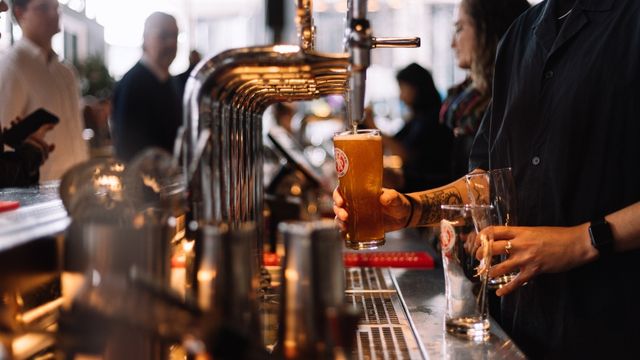 A man pours a pint of beer from a silver tap in a london pub.