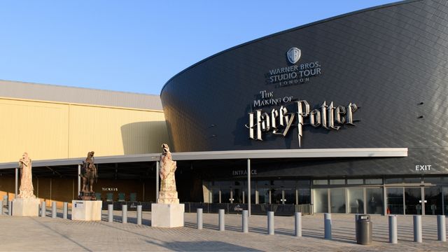 The large black building of the harry potter studios with large statues outside and bright blue sky.