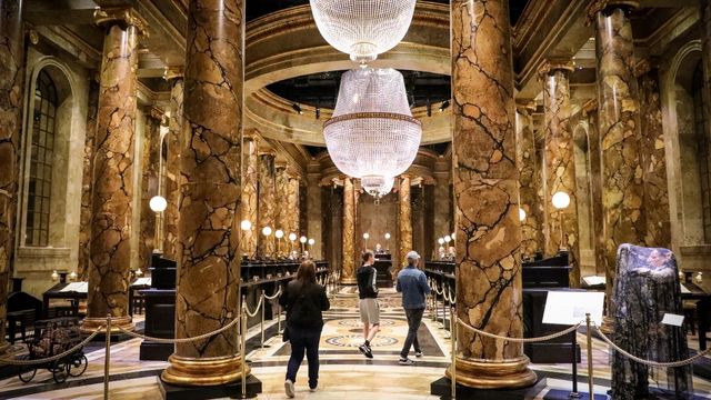 People wander through the golden room of Gringotts Bank at harry potter studios with large pillars and sparkling chandeliers.
