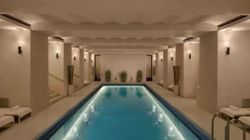 tranquil spa room with cream walls, ceilings and flooring, mood lighting and a long pool with lights in the centre of the room