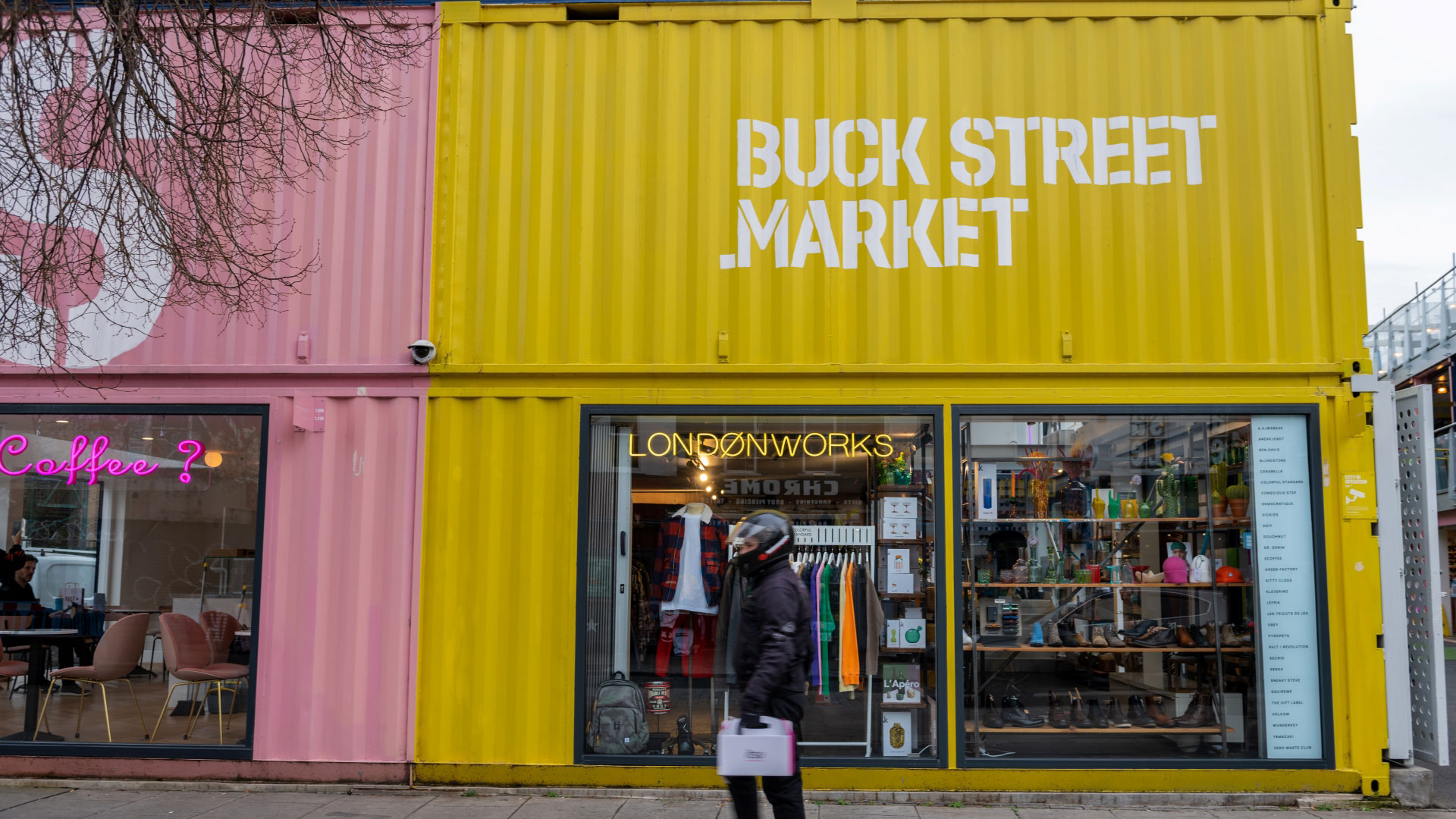 Stop off at Buck Street Market during your visit to Camden, where you'll find independent fashion and food retailers. Credit: Shutterstock. Image courtesy of Shutterstock. Man walking past a bright pink and yellow shipping container with shops inside which has been converted into Buck Street Market