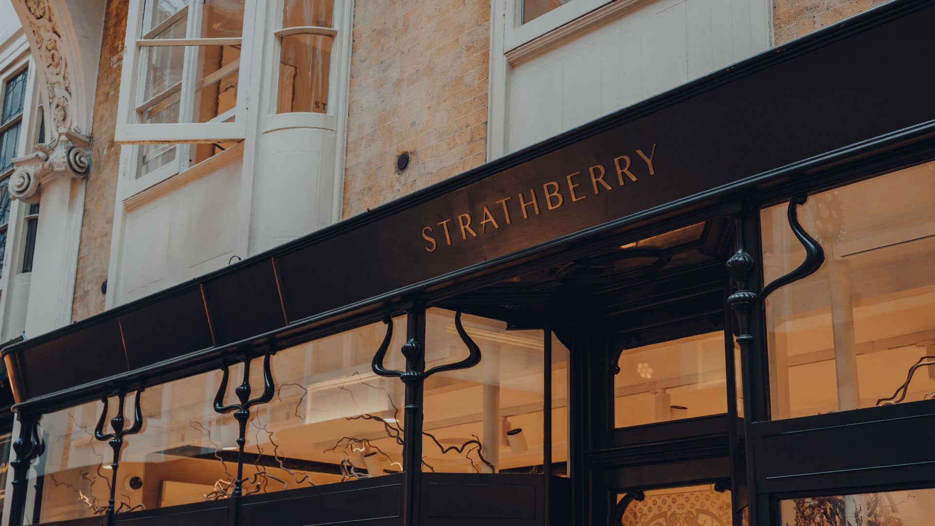 Treat yourself or a loved one with a new handbag from eco-conscious Strathberry. Credit: Shutterstock. Image courtesy of Shutterstock. A black storefront lit up from inside with logo on the front spelling out Strathberry