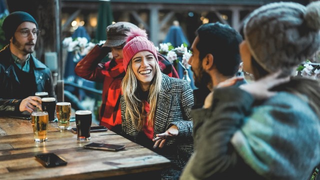 Enjoy a tipple on Christmas Day. © Shutterstock Friends sat around a table with pints on the table in winter clothes and laughing.