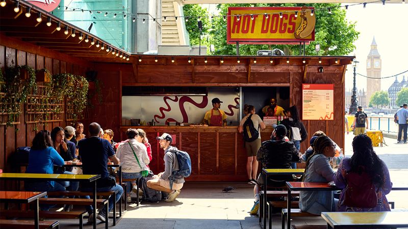 A street food stand serving American-style hot dogs with Big Ben pictured in the background.