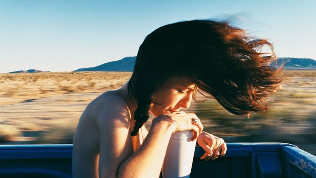 Photograph of woman in trailer of car with hair blowing in the wind.