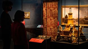 Two people looking at gold sculpture in glass cabinet at Pirates exhibition.