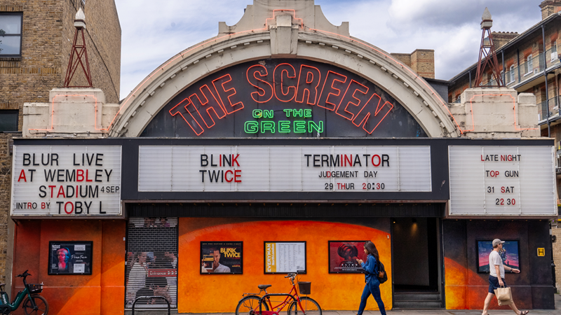 Treat yourself with a visit to Screen on the Green in Islington with its retro feel and mouthwatering food menu. Credit: London & Partners/Peter Cohen. Image courtesy of London & Partners. A photo of the front exterior of Screen on the Green with its red and green neon logo and retro white boards spelling out the names of films on show as people walk passed in the foreground