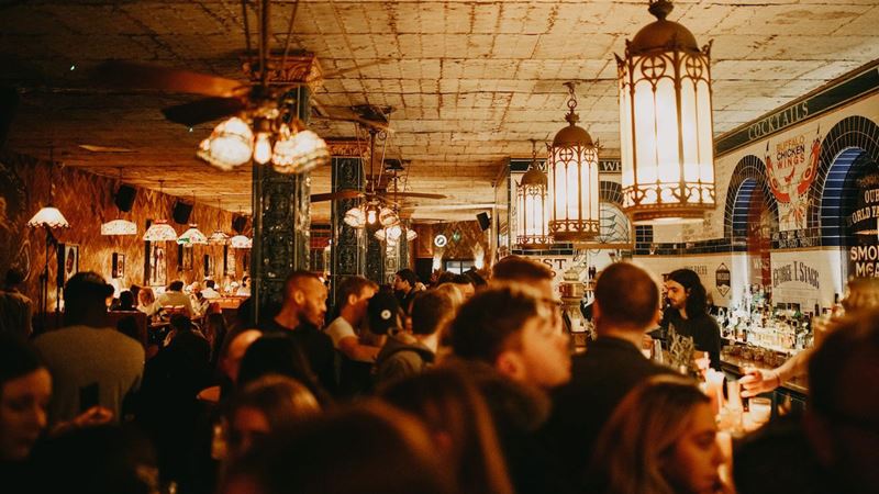 A photo of a crowd of people queuing at the bar at Blues Kitchen in Brixton with eccentric decor and warm lamps illuminating the rooms