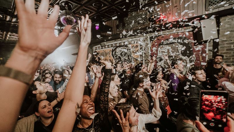 Make memories with your friends at Blues Kitchen in Camden. Credit: Luke O'Brien. Image courtesy of Blues Kitchen. A photo of the crowd at Blues Kitchen in Camden. Everyone is smiling with their hands in the air facing the stage as confetti falls from above