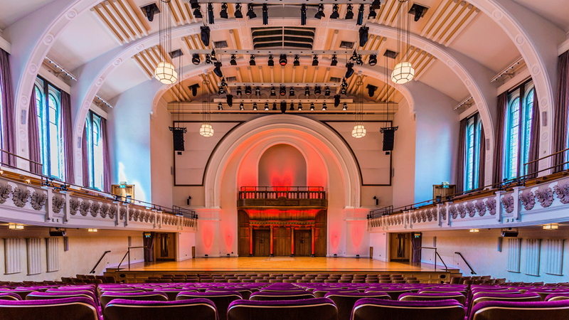 View from the seats facing the stage at Cadogan Hall with red lights illuminating the stage