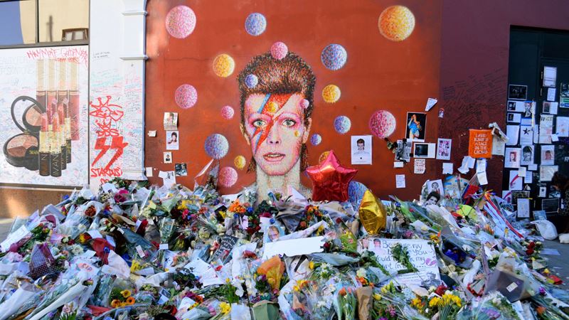 Head to Bowie's old south-London stomping ground where you'll find his famous mural. Credit: Shutterstock. Image courtesy of Shutterstock. Painted mural of David Bowie in Brixton covered with flowers and letters