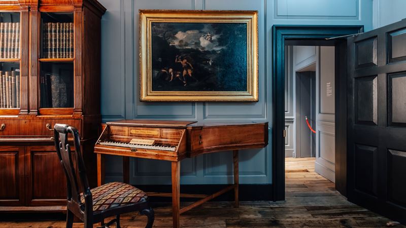 Step inside the world of two gifted musicians at Handel & Hendrix in London. Credit: visitlondon.com/Michael Barrow. Image courtesy of London and Partners. A photo inside one of the rooms at Handel and Hendrix in London with a chair in front of a piano, a wooden bookcase and a large gold framed painting on the wall