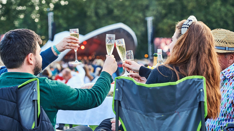 Cheers to the bank holiday weekend at Battersea Park in Concert. Credit: Enable.org. Image courtesy of Enable.org. A family cheers with glasses of champagne sat on camping chairs in front of the stage at Battersea Park in Concert