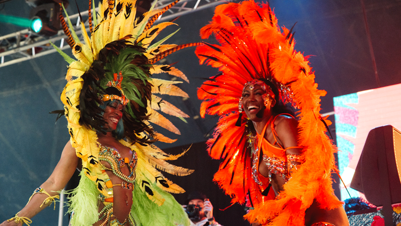 Soak up the good vibrations at City Splash festival. Credit: Garry Jones Photography. Image courtesy of Garry Jones Photography. Two women on stage in bright traditional dress, one in yellow and the other in orange