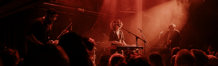 A singer stands in the middle of large crowd with red lights illuminating the room