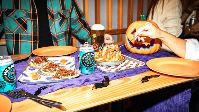 a purple tray with burgers and chips plated, with Halloween decorations on the bench and people reaching in to eat