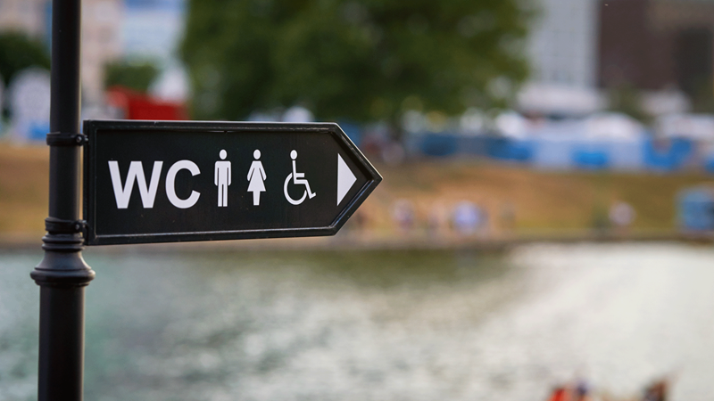 A black sign post with symbols pointing to male female and disabled toilets.
