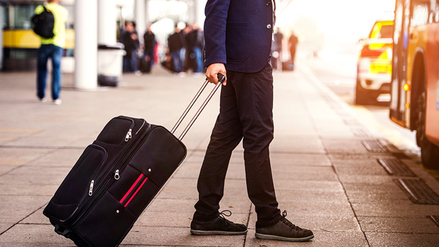 Person walking towards a bus with a suitcase.