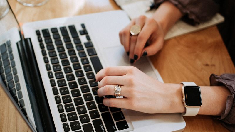 Close up of woman's hand typing on laptop. She wears a smart watch on her wrist.