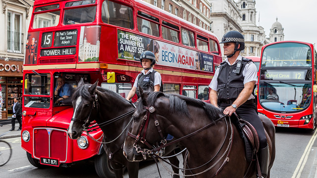 Two police officers on horses ride on a street in London next to a red heritage London Routemaster