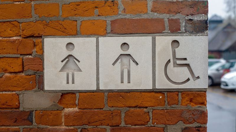 A photo of a toilet sign with female, male and disabled icons on a brick wall in London