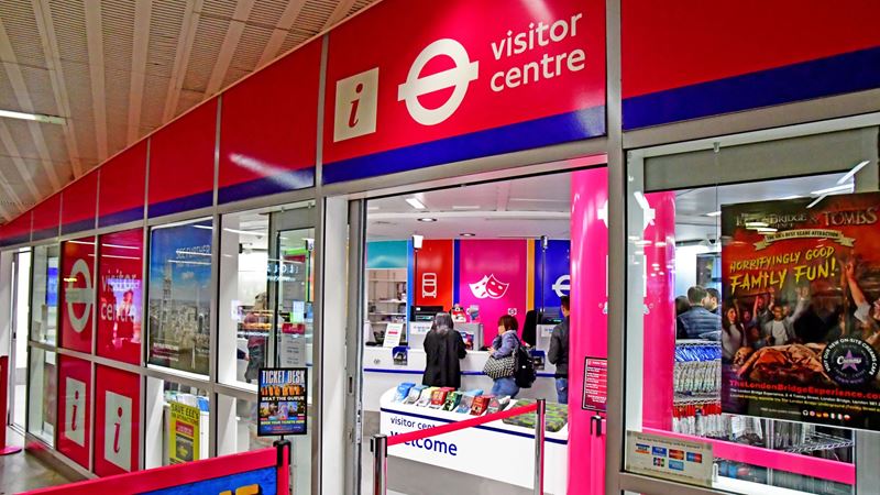 London visitor centre's red and blue shopfront, with people queuing inside.