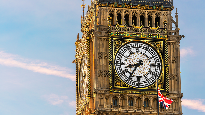 British Union flag in front of the clock face of Big Ben in London on a sunny day