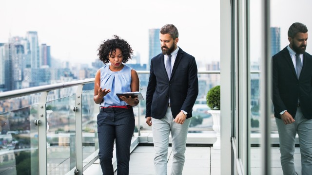 A portrait of two businesspeople walking on a glass balcony with the London city skyline shown below.