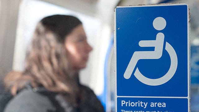 Transport for London and train companies offer passenger assistance. Image courtesy of Shutterstock. Woman sitting on the London Underground behind a sign with a wheelchair symbol that says "Priority area"