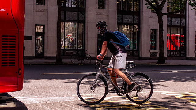 Cycling and public transport in London. Image courtesy of Shutterstock. A man cycling behind a red London bus.