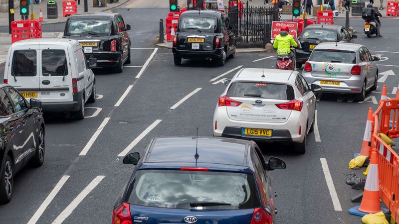 A photo from above of cars and taxis sat in car lanes at traffic lights in London
