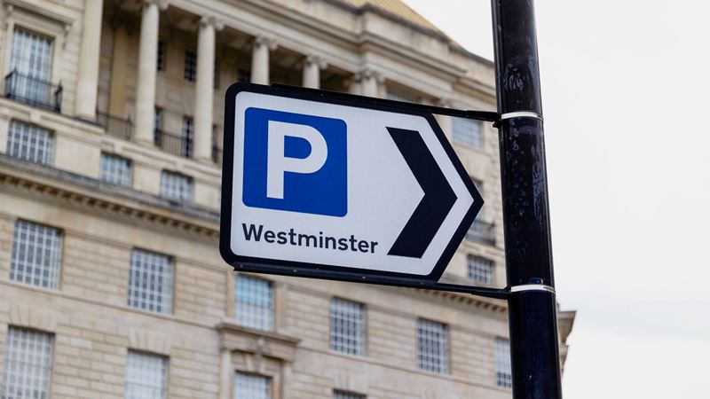 A photo of a car parking sign with Westminster written below it on a street in London with a building in the background