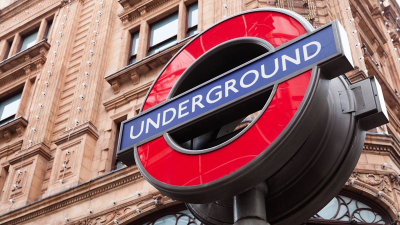 A close-up photo of the London Underground roundel outside a station with a building in the background