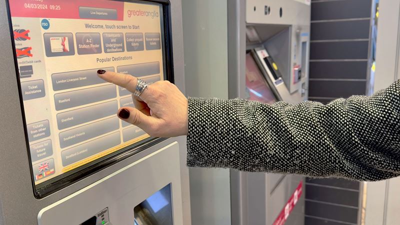 A photo of a woman's finger touching the buttons on a touchscreen ticket machine at a train station