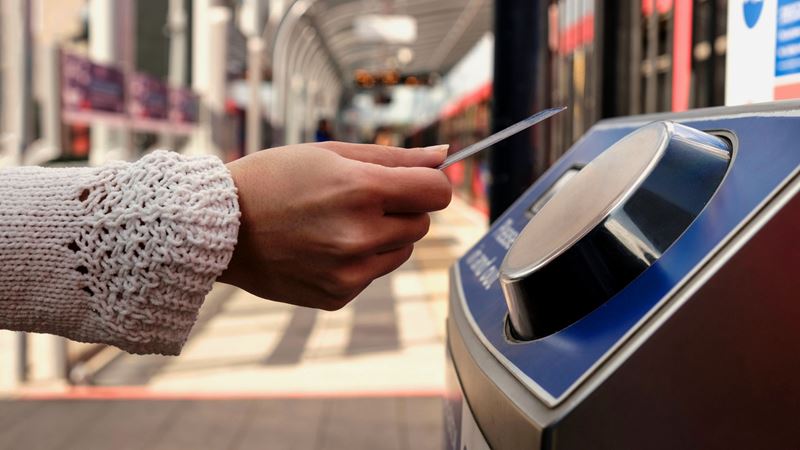 Tap in and out of stations easily with a contactless Oyster card. Credit: Shutterstock. Image courtesy of Shutterstock. A photo of a womans hand holding a contactless card against a London Underground train ticket reader