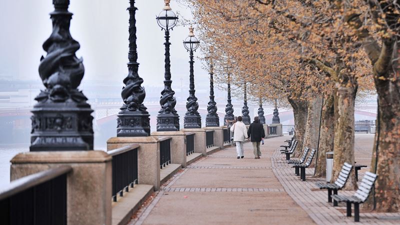 Take in London's famous sights during a wander along the river Thames. Credit: Shutterstock. Image courtesy of Shutterstock. A photo of two people walking along a path next to the river Thames with the iconic black fish lampposts lining the side
