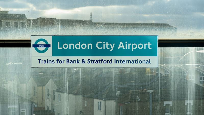 Hop on a DLR train from London City Airport towards Bank and Stratford. Credit: Shutterstock. Image courtesy of Shutterstock. A photo of a DLR sign on a train platform including a DLR roundel and London City Airport trains for Bank and Stratford International written on it