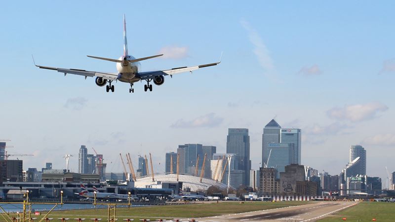A photo of an airplane landing on the runway at London City Airport with the City of London skyline in the background