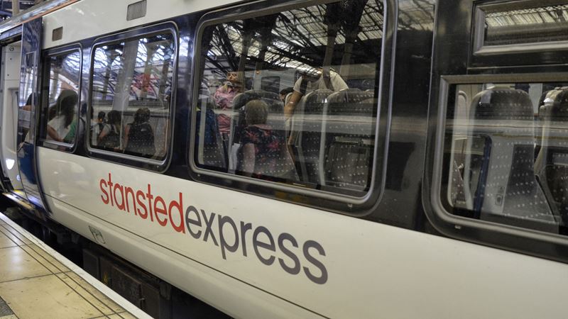 Board the Stansted Express for quick and easy travel into London. Credit: Shutterstock. Image courtesy of Shutterstock. A photo of a Stansted Express train stopped at a platform with a view of people sat on chairs through the windows