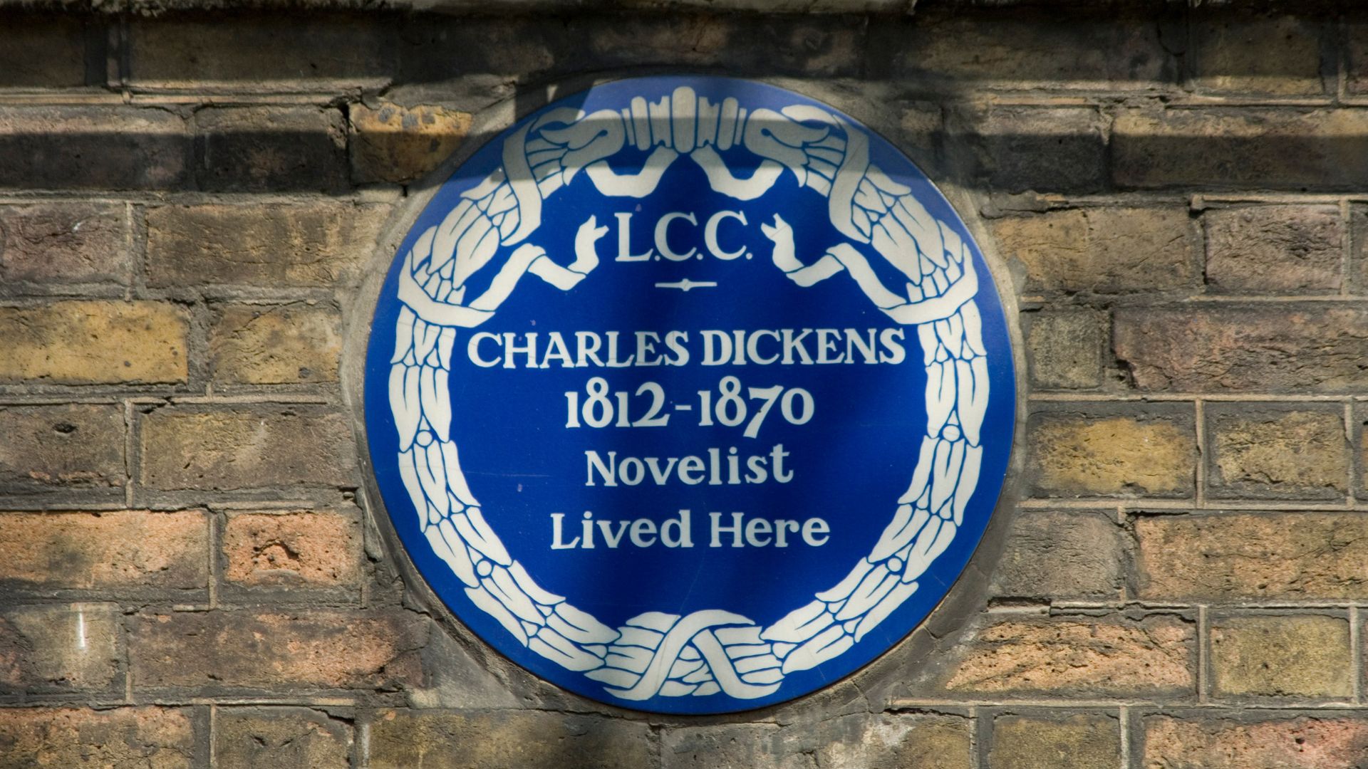 Charles Dickens Blue Plaque. © English Heritage A round blue plaque with evidence of Charles Dickens' residence on a brick wall in London.