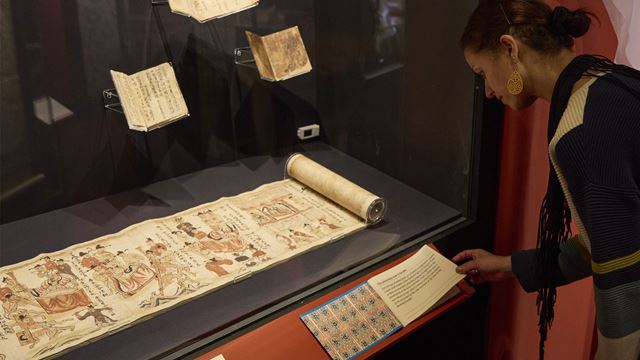 Woman reading an information sheet below a scroll at the British Library exhibition.