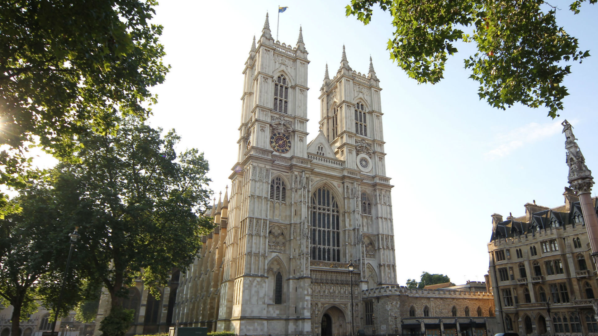 Westminster Abbey exterior. Photo: Andrew Dunsmore. Image courtesy of Sutton PR. Exterior view of Westminster Abbey with leafy trees and sunshine